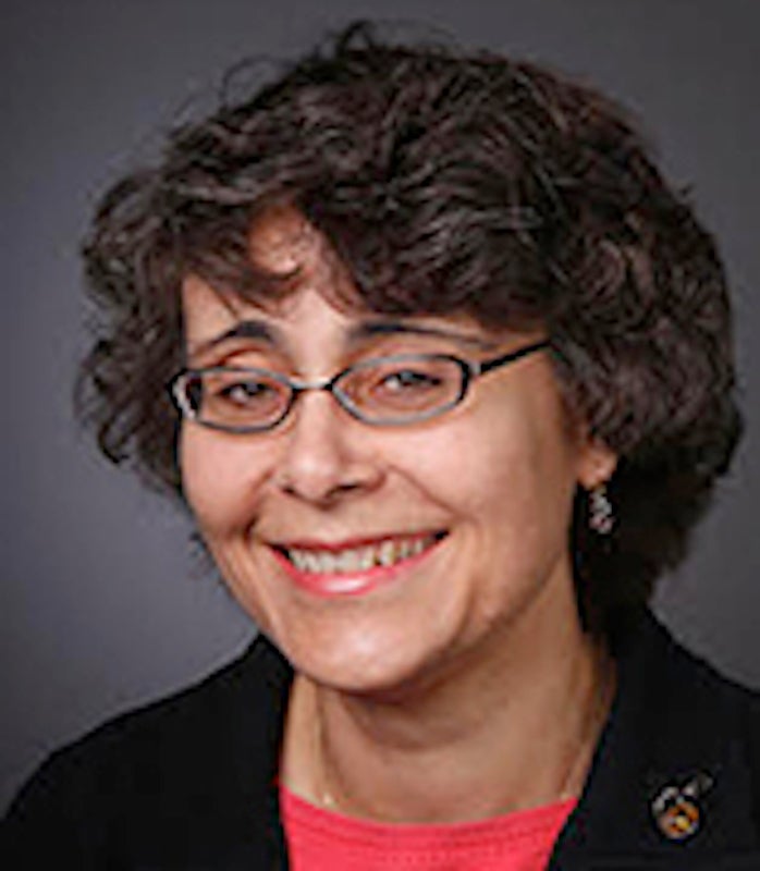 woman in a red blouse and black blazer with glasses, smiling.